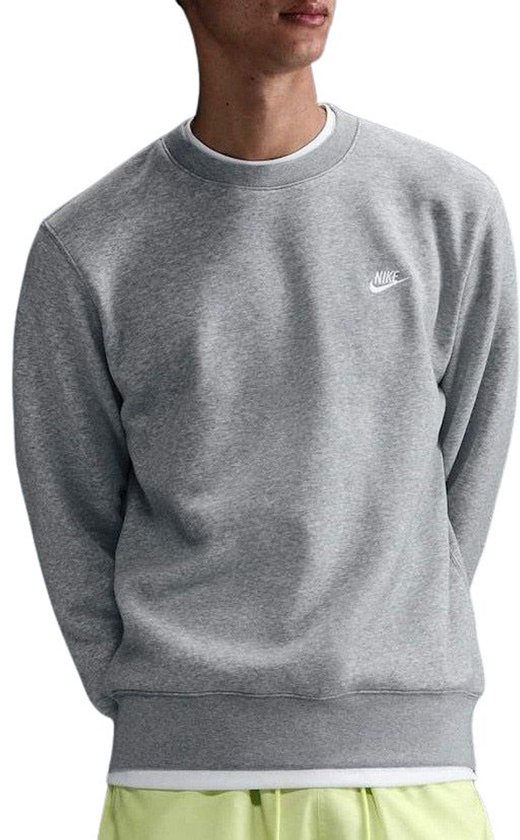 Man draagt een grijze Nike sweater met een witte T-shirt eronder en lichtgele shorts.