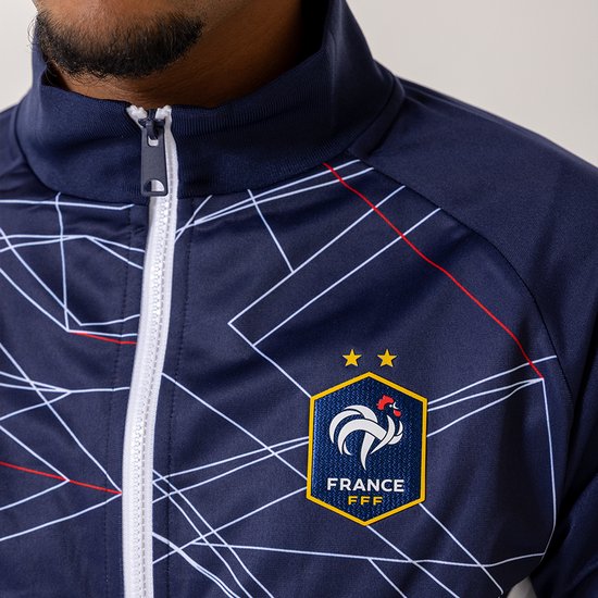 Close-up van een donkerblauwe trainingsjas met FFF-logo, geometrisch patroon en witte rits.