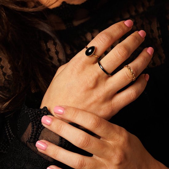 Handen met roze nagellak, met sieraden: een ring met zwarte steen, een smalle zwarte ring en een gouden schakelring.