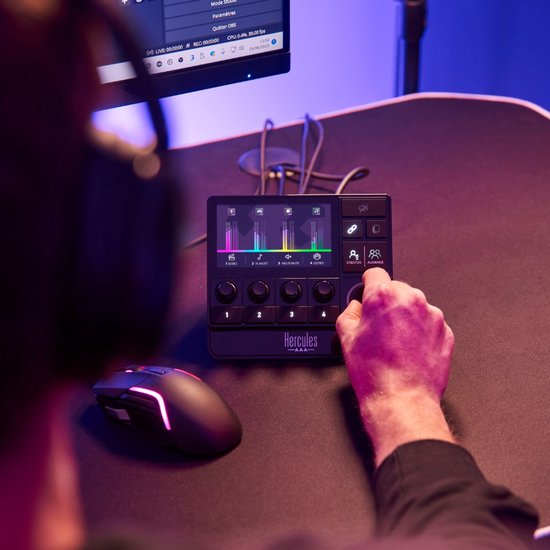 Een hand draait aan de knop van een zwarte Hercules audiocontroller, naast een game-muis.