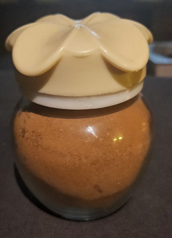 Glazen pot met kaneelpoeder en een crème kleurige deksel in bloemvorm.