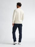 Man met rug naar voren, draagt een beige sweater en donkerblauwe cargobroek.