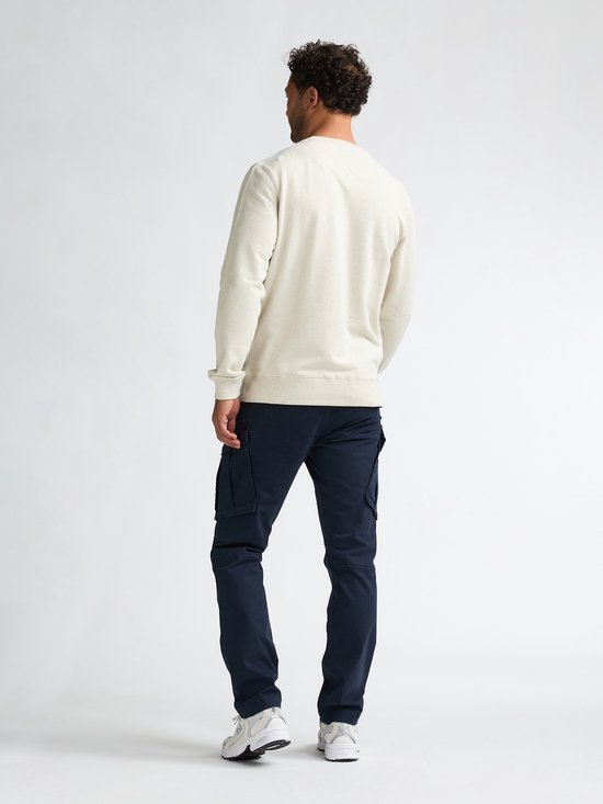 Man met rug naar voren, draagt een beige sweater en donkerblauwe cargobroek.