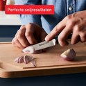 Handen snijden rode ui met Tefal mes op snijplank
