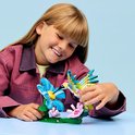 Une fille portant une veste rose regarde un colibri LEGO qui boit du nectar d'une fleur bleue.