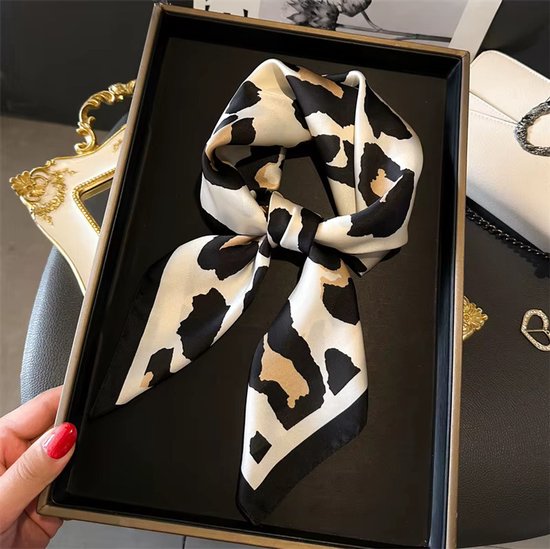 Vierkante sjaal met luipaardprint in ivoor, camel en zwart, met zwarte rand, gestrikt. De sjaal wordt door een hand met rode nagellak vastgehouden.