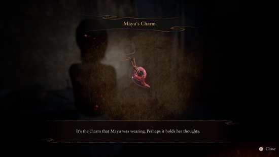 Een rood, amuletachtig object 'Mayu's Charm' hangt in het midden, met een wazige achtergrond.