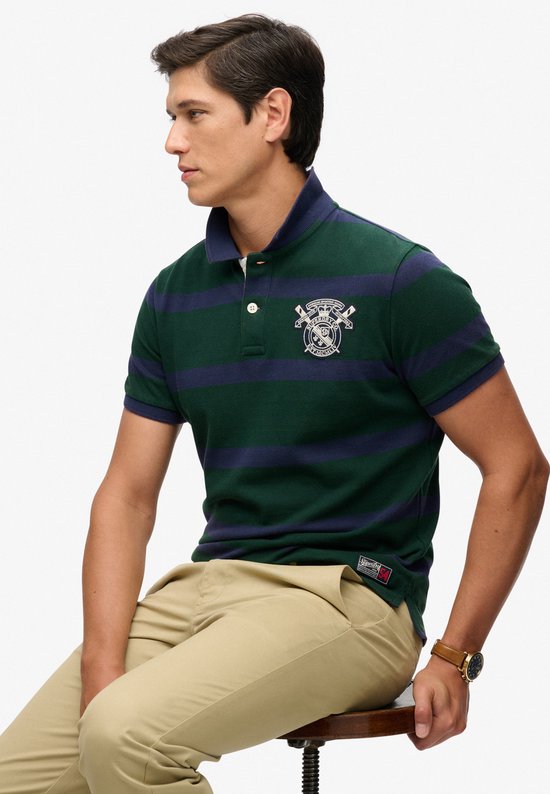 Man zittend, draagt een donkergroene polo met marineblauwe strepen, geborduurd logo.