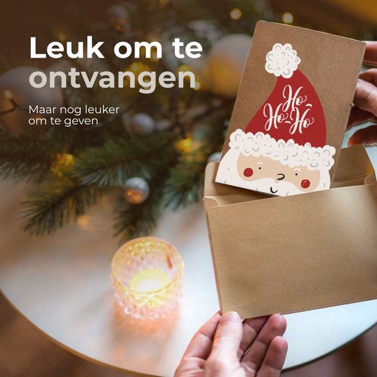 Kerstkaart met kerstman design wordt uit envelop gehaald, kerstboom en kaarslicht op achtergrond.