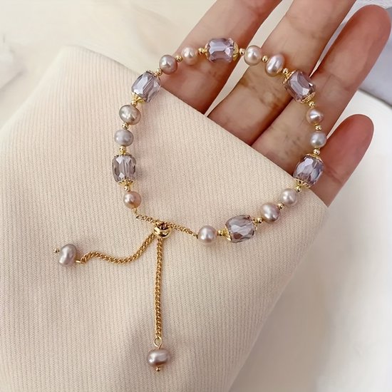 Gouden armband met roze parels en grijze facetkralen gedragen door een hand. Verstelbaar met gouden ketting.