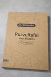 Grijze kartonnen verpakking van DUTCHERS Puzzeltafel met 6 lades voor 1000 stukjes, met topografische kaartprint.