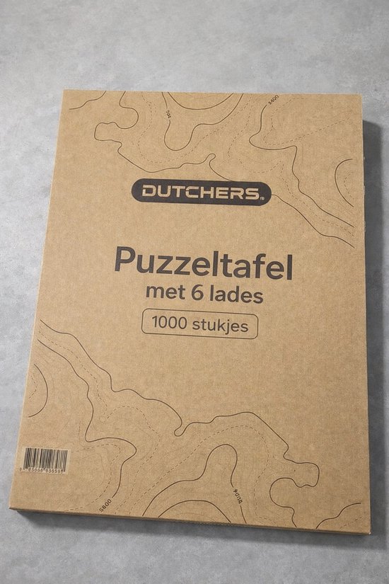 Grijze kartonnen verpakking van DUTCHERS Puzzeltafel met 6 lades voor 1000 stukjes, met topografische kaartprint.