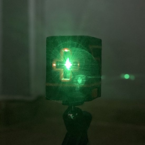 Groene laserprojector die een kruis op een donkere achtergrond projecteert.