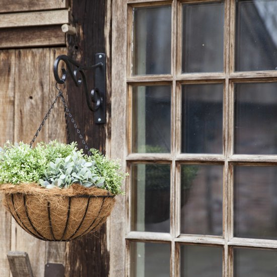 Hangende bloempot met kettingen aan een houten schuur. Gevuld met groene planten.