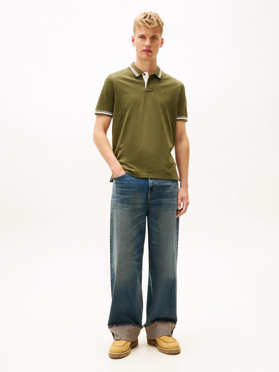 Man met blond haar draagt een olijfgroene polo en jeans.