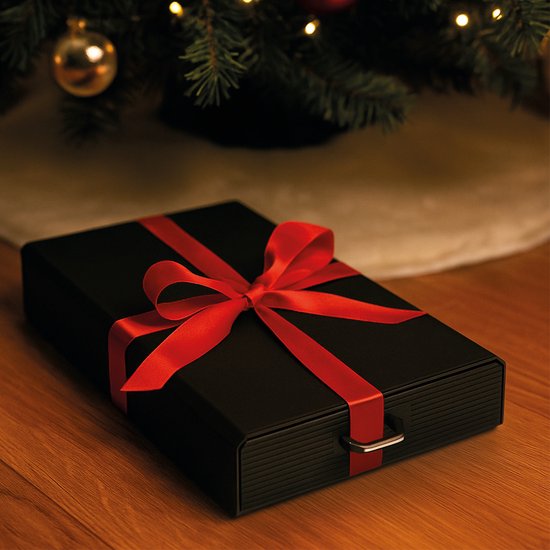 Boîte noire pour capsules, emballée avec un ruban rouge comme cadeau sous un sapin de Noël.