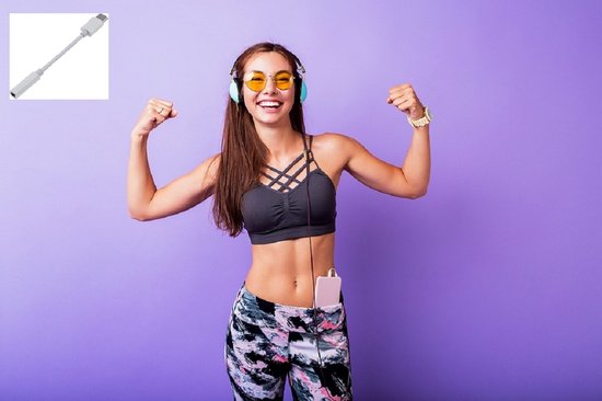 Vrolijke vrouw in sportkleding met koptelefoon, zonnebril en sieraden, die haar spieren spant.