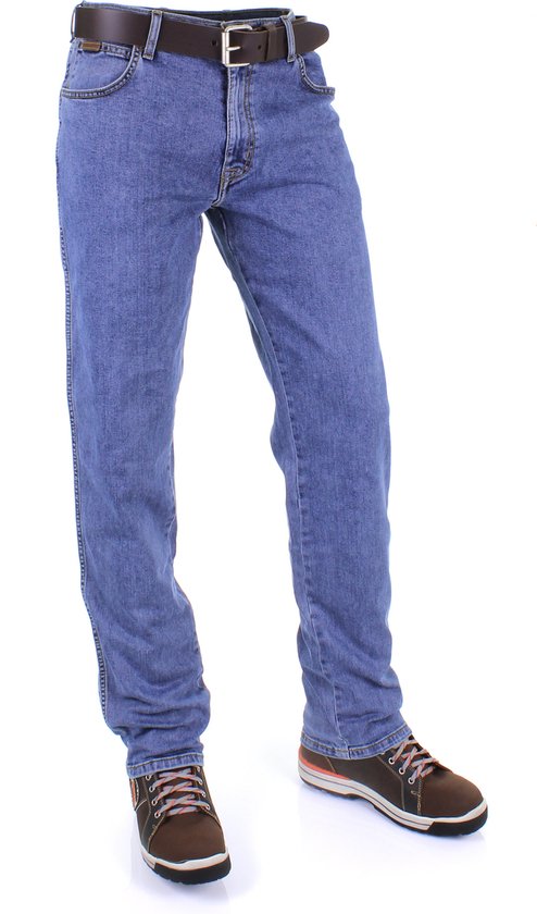 Een taille-omhoog opname van een model in een blauwe Wrangler jeans, met een bruine riem en bruine schoenen.