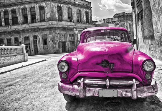 Une voiture vintage rose avec des détails chromés dans une rue de ville avec de vieux bâtiments.