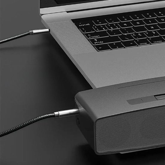 Câble audio noir reliant un ordinateur portable à un haut-parleur gris. Texture tressée.