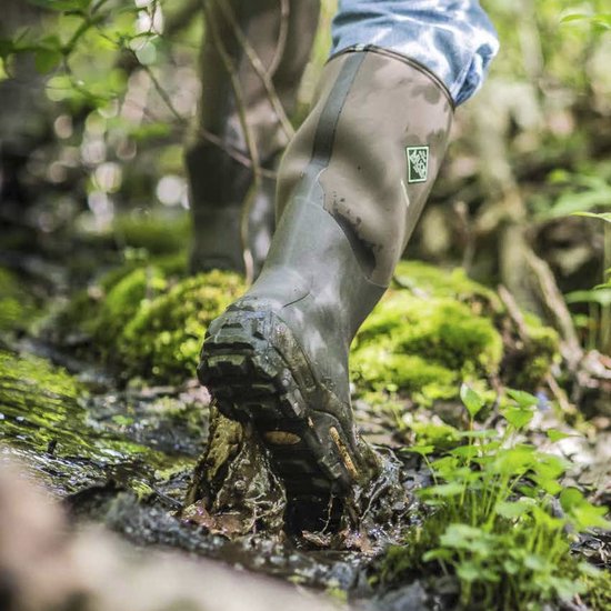 Een persoon draagt een groene Muck Boot Muckmaster laars in modderig terrein.