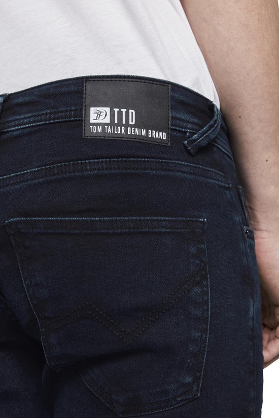 Close-up van het zwarte leren label op de achterkant van een donkerblauwe jeans met 'TOM TAILOR DENIM BRAND'.