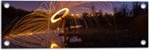 Tuinposter – Man met Lichtsnoer op Keien langs Rivier - 60x20 cm Foto op Tuinposter (wanddecoratie voor buiten en binnen)