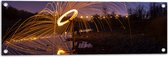 Tuinposter – Man met Lichtsnoer op Keien langs Rivier - 90x30 cm Foto op Tuinposter (wanddecoratie voor buiten en binnen)