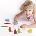 Een jong meisje met blond haar ligt op de grond en kleurt met een blauwe potlood, Peppa Pig stempels liggen op de tafel.