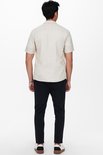 Man van achteren gezien, met een beige linnen mix overhemd met korte mouwen en een zwarte broek.