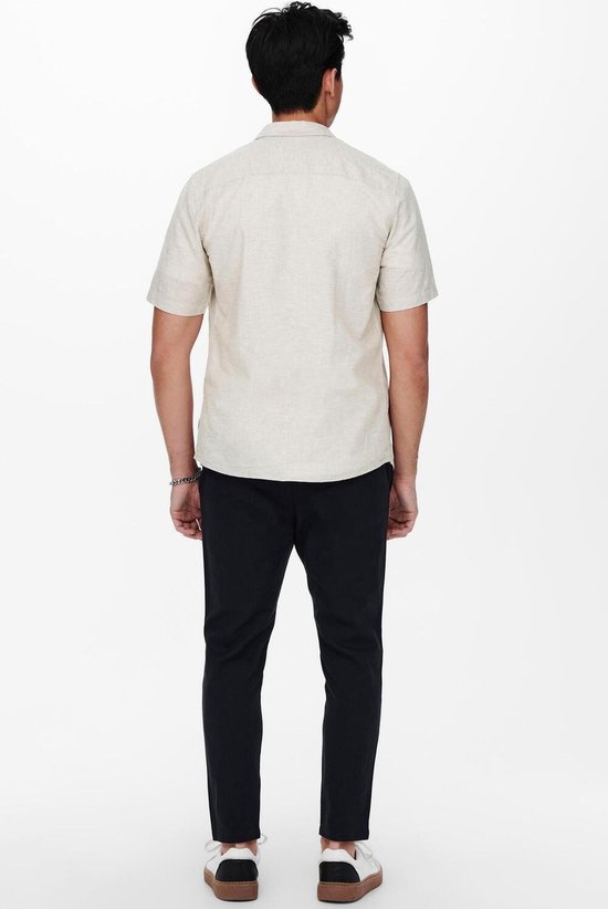 Man van achteren gezien, met een beige linnen mix overhemd met korte mouwen en een zwarte broek.