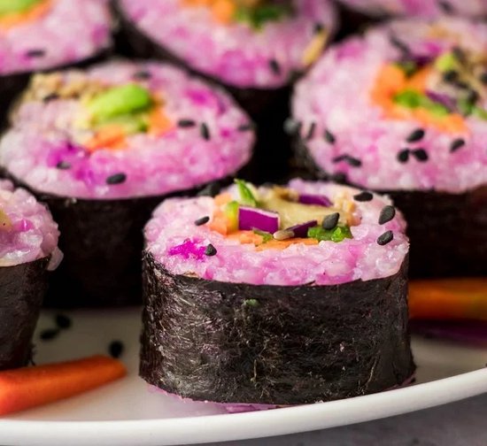 Sushirolletjes met roze rijst, groenten en zwart sesamzaad.