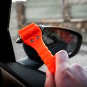 Hand houdt oranje veiligheidshamer met zilveren punt bij een autospiegel.