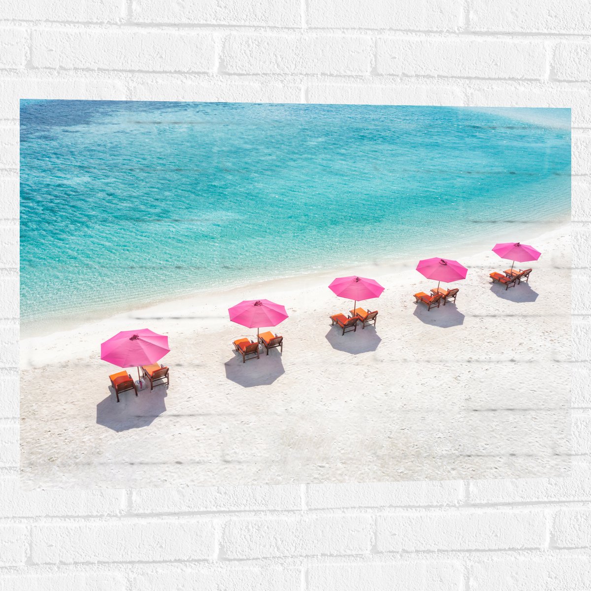 Muursticker - Ligbedden onder Roze Parasols op het Witte Strand bij Blauwe Oceaan - 80x60