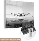MuchoWow® Glasschilderij 120x90 cm - Schilderij glas - Vliegtuig landt op Schiphol - zwart wit - Foto op acrylglas - Schilderijen