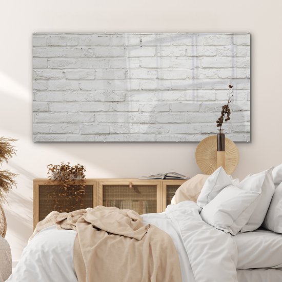 Acrylglas schilderij met witte baksteen textuur, hangend boven een houten nachtkastje in een slaapkamer met een wit bed.
