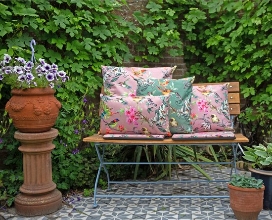 Kussens met bloemen- en vogelprint in het groen en roze, op een houten tuinbank.