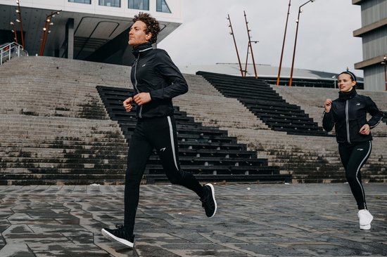 Man en vrouw in zwarte Avento sportkleding rennen buiten, met reflecterende strepen.