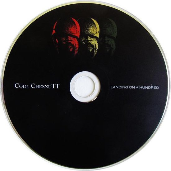 CD met zwart label, titel "Landing On A Hundred" en "Cody Chesnutt". Drie rode, gele en groene portretten boven de tekst.