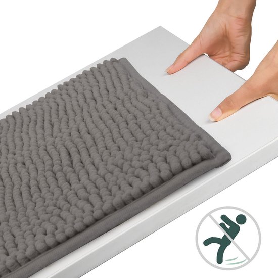 Grijze badmat met een zacht, bolletjespatroon, liggend op een witte plank met een antislip-symbool.