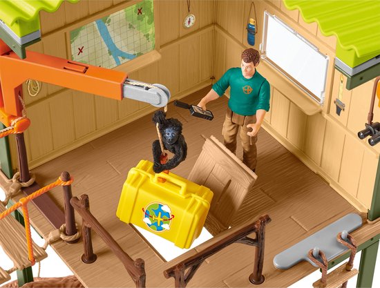 Binnenkant van een speelgoed station met een verzorger, gorilla aan een kraan, een gele koffer en een kaart aan de muur.