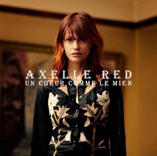 Axelle Red aux cheveux roux, portant une chemise noire à imprimé floral blanc. Texte : "AXELLE RED UN COEUR COMME LE MIEN".