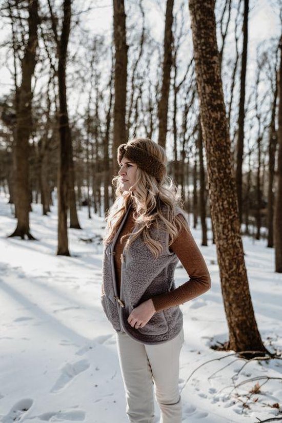 Vrouw in winterlandschap met een lichtgrijze teddy bodywarmer, bruine coltrui en crème broek.