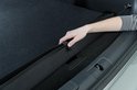 Hand rolt zwarte bumperbeschermer op in kofferbak van zilveren stationwagen.