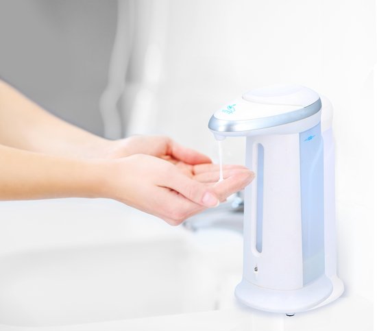 Witte automatische zeepdispenser in gebruik, met een zilveren rand en een transparant reservoir.