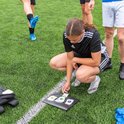 Meisje in zwart sporttenue kijkt naar kaarten op donkere ondergrond, met andere spelers.