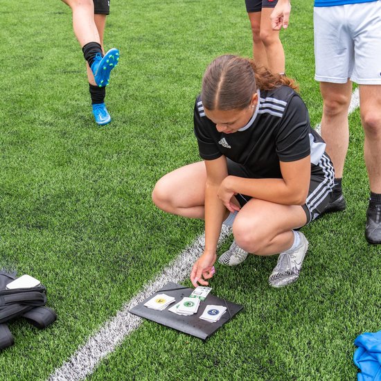 Meisje in zwart sporttenue kijkt naar kaarten op donkere ondergrond, met andere spelers.
