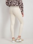 Achterkant model in een lichte, skinny jeans met rafels aan de onderkant en beige sneakers.