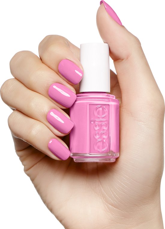 Hand met gelakte nagels in fel roze, met een flesje Essie nagellak.