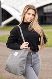 Mannequin aux cheveux blonds, pull noir à col roulé et jean gris porte un sac gris en velours côtelé sur son épaule.